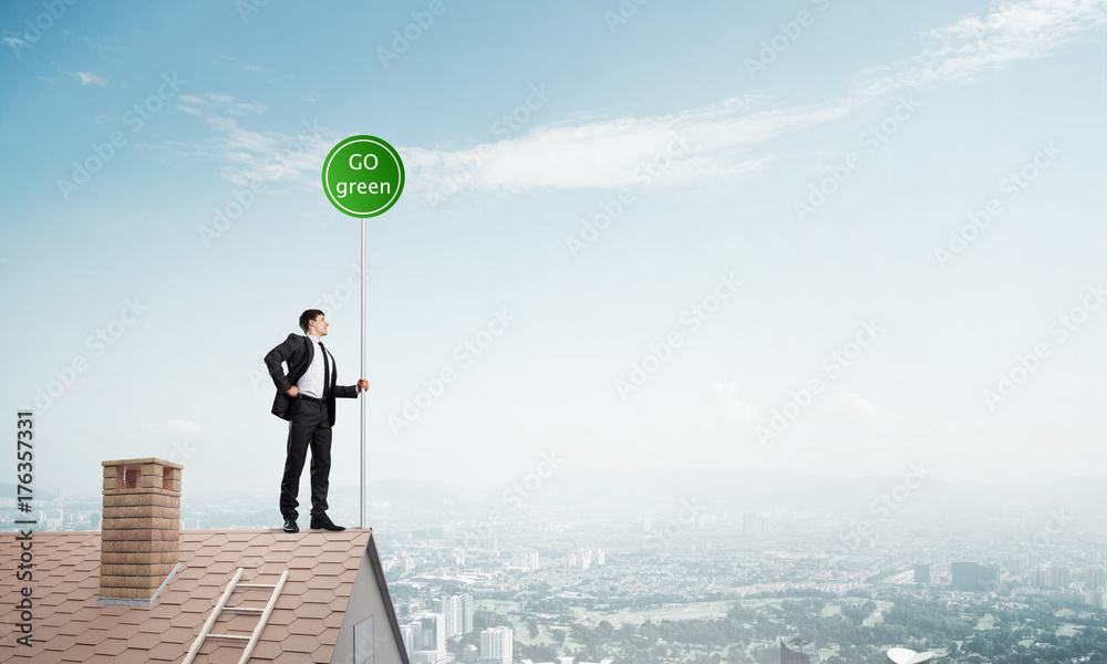 Businessman in suit on house top with ecology concept signboard. Mixed media Businessman in suit on house top with ecology concept signboard. Mixed media