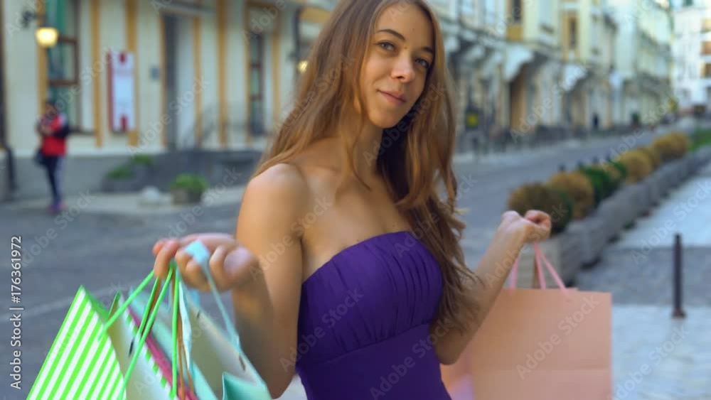 close-up portrait of a girl in front of a boutique. The girl holds bright colored paper bags of their shop in her hands and smiles sweetly. presses purchases to the face 4K