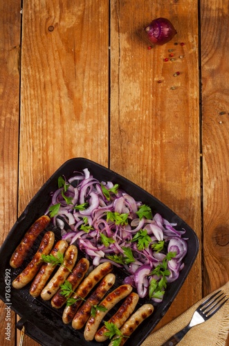 Fried sausages with onion and parsley in a pan on wooden background