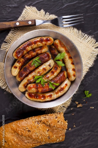 Fried sausages with parsley, bread and fork in a pan on black background