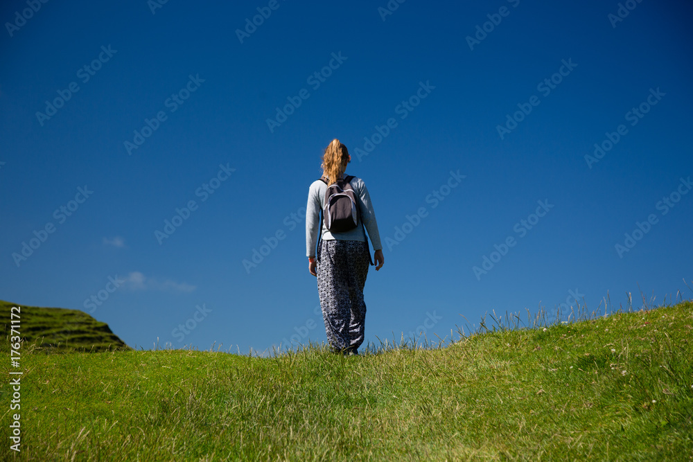 Young blonde girl walks outdoors, on grass covered field