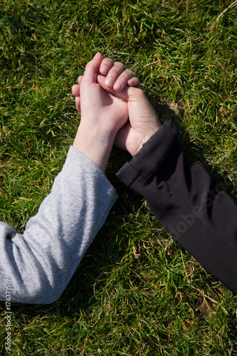 Two female hands, mother and saughter holds each other hands lying in grass