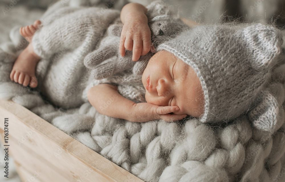 Tiny baby in grey clothes sleeps on woolen blanket in the box Tiny baby in grey clothes sleeps on woolen blanket in the box