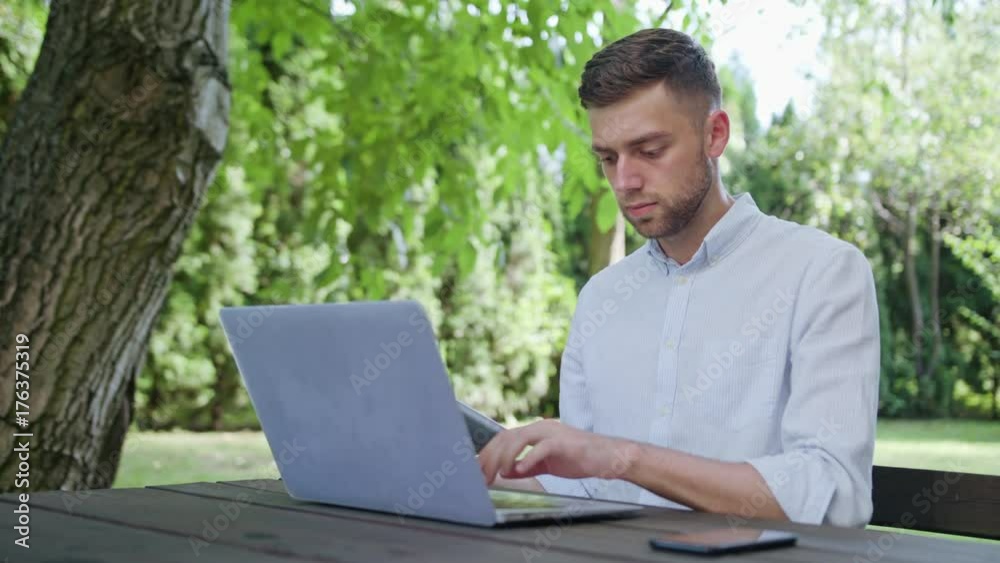 A young man using a laptop and a tablet in the park. Medium shot. Soft Focus A young man using a laptop and a tablet in the park. Medium shot. Soft Focus