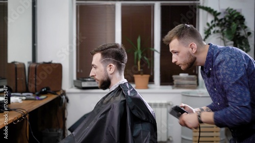 Barber stylist making hair to male customer sitting in barbershop