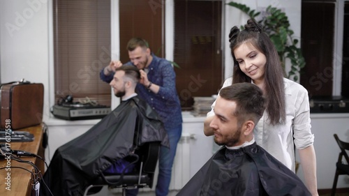 Professional hairdressers making stylish hairdo to men sitting in salon
