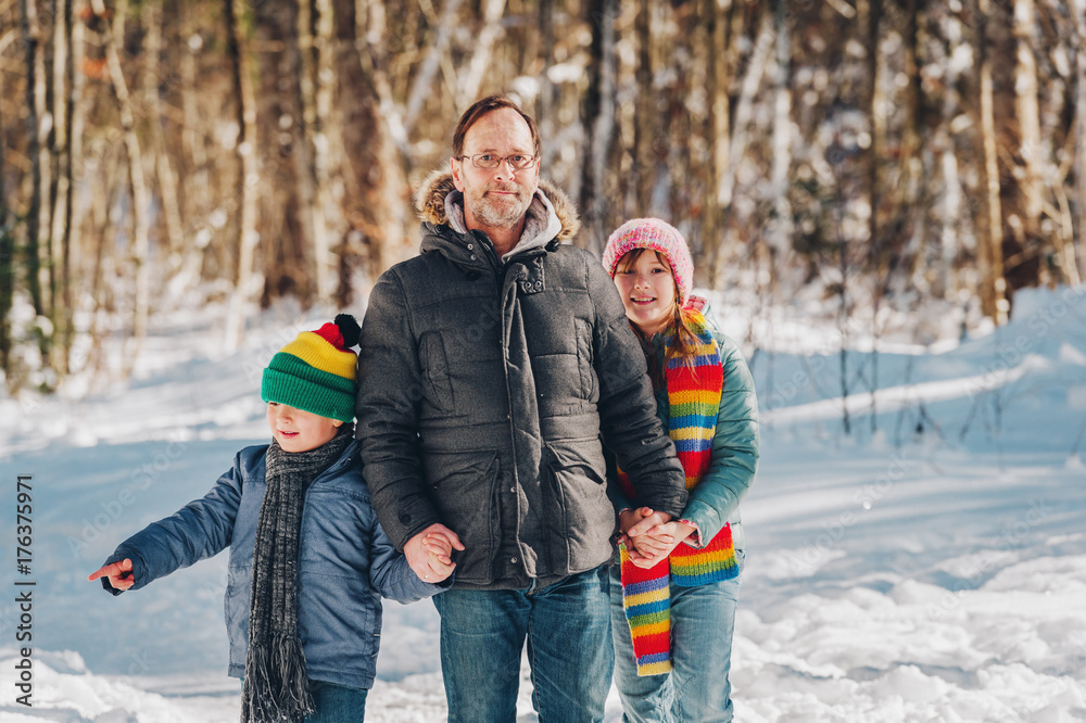 Portrait of father and two kids enjoying winter forest on a nice sunny day