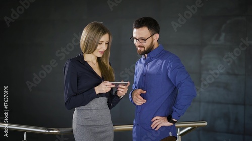 Office workers browsing smartphone. Cheerful male and female entrepreneurs standingin office and using smartphone while coworking. photo