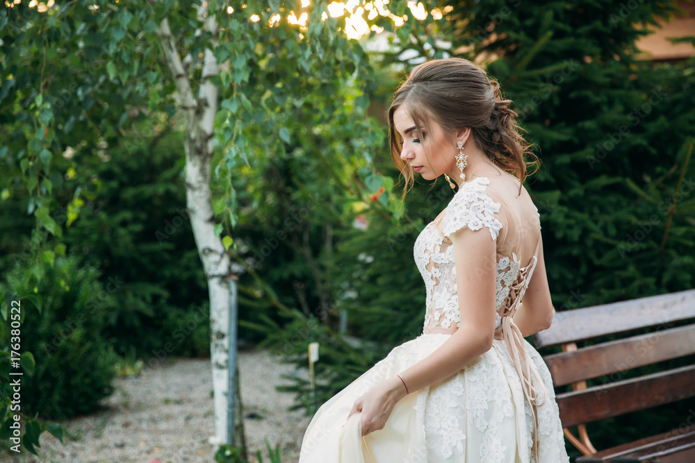 Young girl in wedding dress in park posing for photographer. Sunny weather, summer. Young girl in wedding dress in park posing for photographer. Sunny weather, summer.