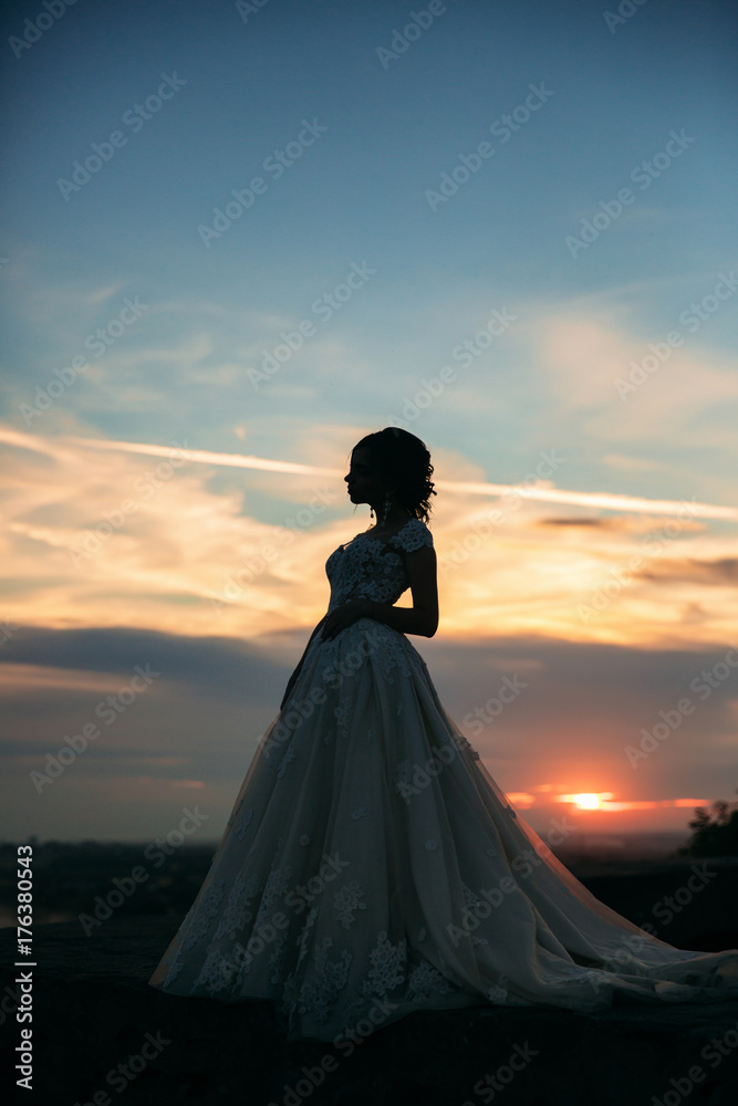 Young girl in wedding dress on city background at sunset. Summer