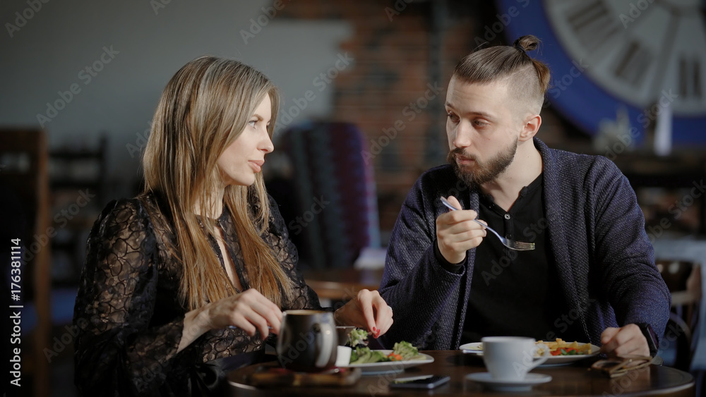A young couple eating a salad in a restaurant, a man and a pretty woman talking during a meal, on the table are cups of coffee