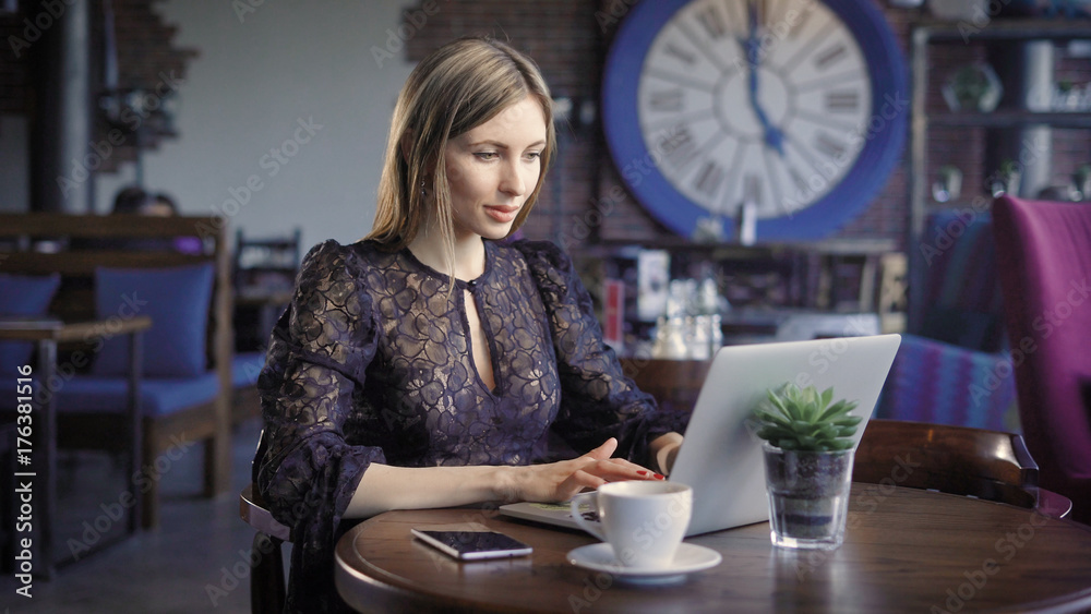 A woman who sits in a lonely restaurant during the day looks at a dating site on a laptop, responding to fan messages, next to her is a cup of coffee A woman who sits in a lonely restaurant during the day looks at a dating site on a laptop, responding to fan messages, next to her is a cup of coffee