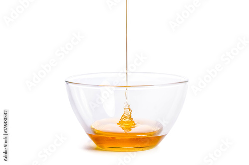 Pouring honey into a glass bowl on a white background