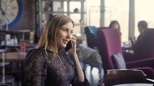 Beautiful smiling female talking phont. Young smiling female in elegant dress talking phone while sitting in cafe.