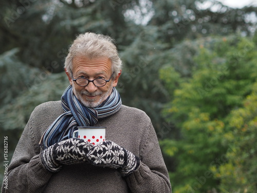 Bärtiger Mann mit Schal und Handschuhen genießt eine Tasse heißen Tee