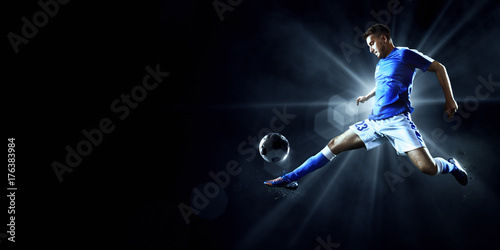 Fototapeta Piłkarz wykonuje akcję akcji na ciemnym tle. Gracz ma na sobie niemarkowy mundur sportowy.