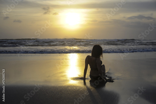 silhouette of young woman lying on sand looking to sea sunset horizon with beautiful sun