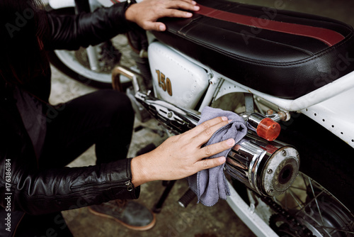 Close-up shot of unrecognizable biker wearing black leather jacket polishing motorcycle while sitting on haunches
