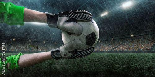 Soccer goalkeeper catches a ball on big professional football arena. Goalkeeper wears unbranded sport uniform.
