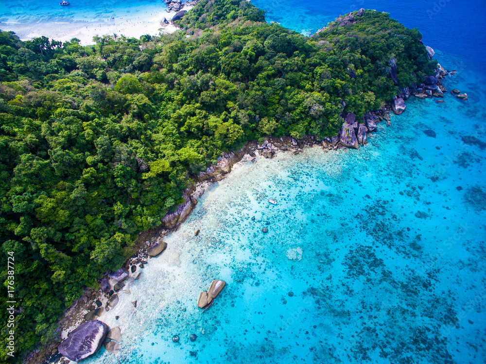 Top aerial view of isolated beautiful tropical island with white sand beach, blue clear water and granite stones. Also top view of speedboats above coral reef. Similan Islands, Thailand.