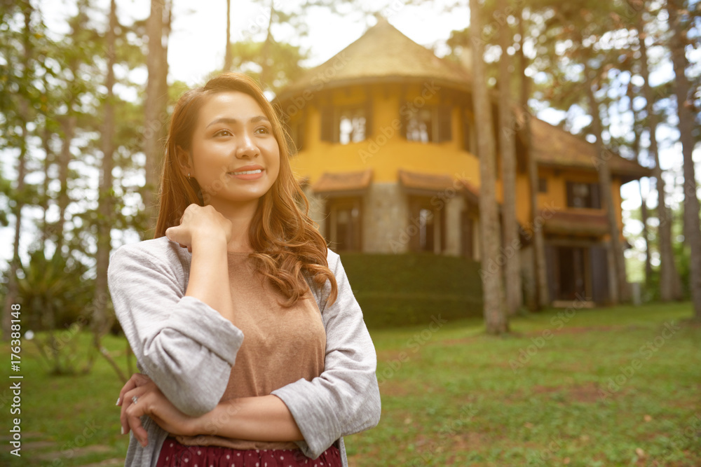 Portrait of smiling Asian woman posing in front yard of her countryside house in sunlight
