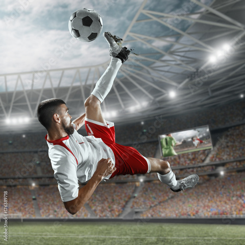 Fototapeta Piłkarz wykonuje grę akcji i bije piłkę na profesjonalnym stadionie. Gracz ma na sobie niemarkowy mundur sportowy.