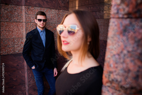 Man and woman in black sunglasses stand before marble wall
