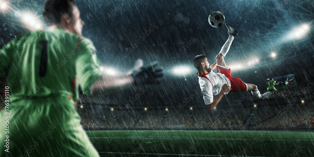 Soccer player scores the ball into the goal on professional rainy stadium. The goalkeeper protects the football gate. Players wears unbranded sport uniform.