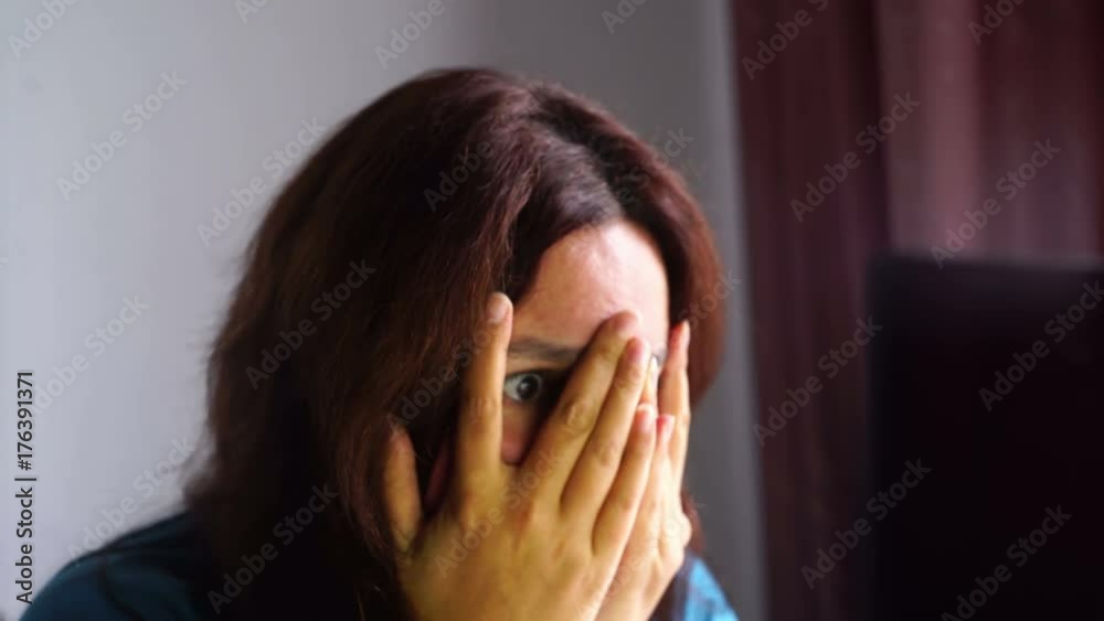 natural beauty brunette woman in front of computer watching scary movie, hide in fingers, affraid expression