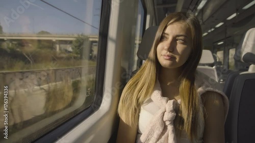 Beautiful young girl seats in the wagon of the train dreaming looking at the window and listening to the music in the headphones