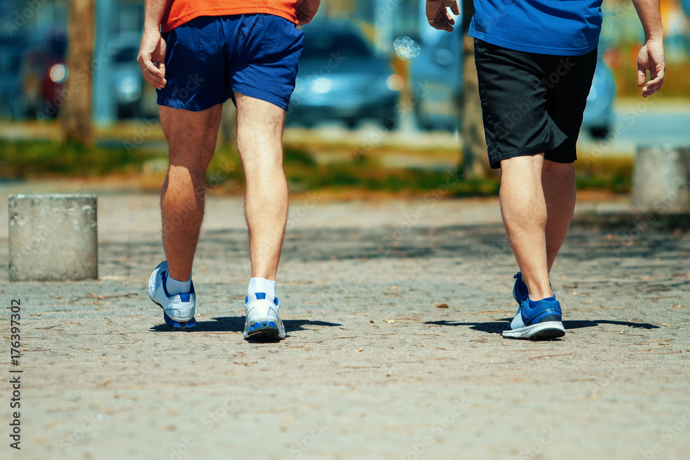 Two men seen from behind walk exercising on a park path Two men seen from behind walk exercising on a park path