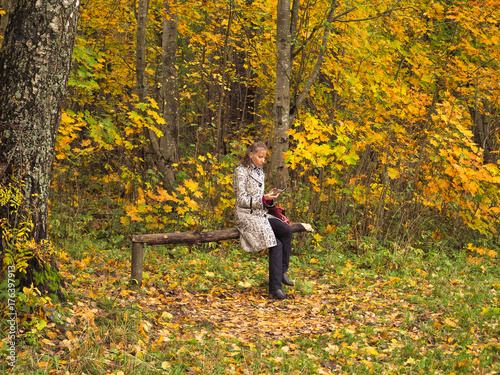 A woman sits in autumn Park with a mobile phone.