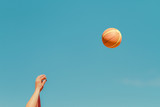 Man's arms against blue sky while throwing a basketball
