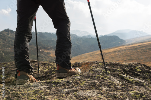 Close-up of male legs in trekking boots with sticks for Nordic walking against the background of rocks and distant Caucasian lands