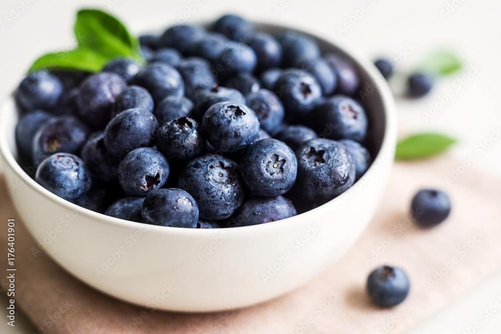 Juicy and fresh blueberries with green leaves on white bowl. Healthy eating Juicy and fresh blueberries with green leaves on white bowl. Healthy eating