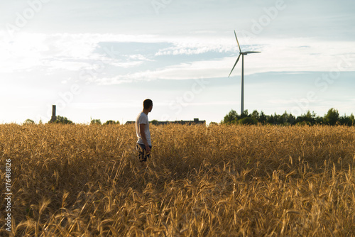 A man standing in a field looking at a wind generator