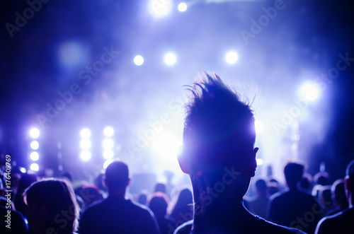 silhouettes of concert crowd and mohawk punk hair style in front of bright stage lights