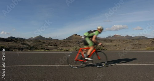 A Road Cyclist Peddles along a road with Volcanos in the background.