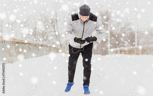 man with earphones and cellphone running in winter
