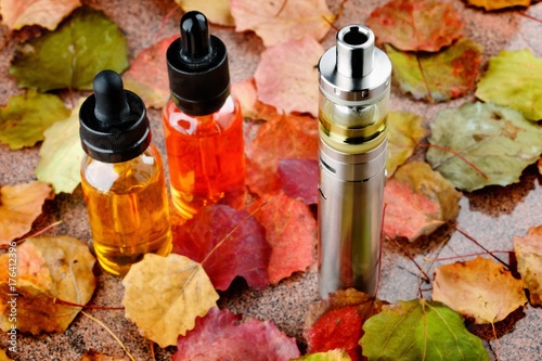 Electronic cigarette and vape liquids on wooden table with autumn leaves
