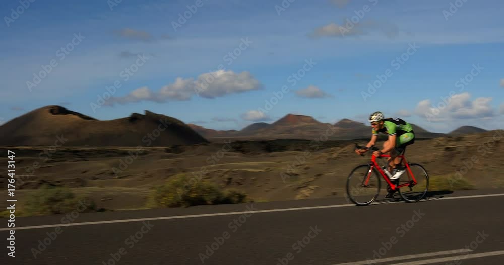 A Road Cyclist Peddles along a road with Volcanos in the background. A Road Cyclist Peddles along a road with Volcanos in the background.