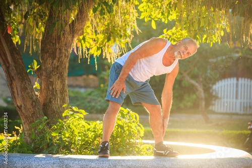 Old Man Does Morning Exercises Bends Body to Foot on Barrier