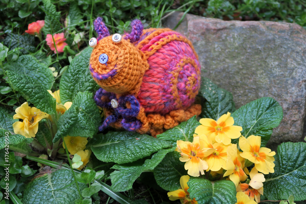 crochet pink snail on twig with primroses in springtime