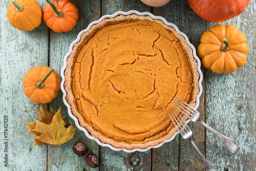 Traditional homemade open pumokin pie decorated with bright orange pumpkins and marple leaves on blue wooden background photo