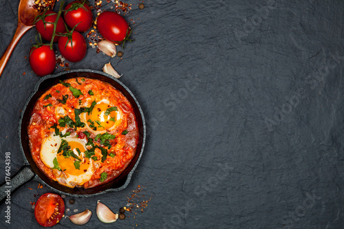 Breakfast. Shakshuka with bread in pan on a black rustic background. Fried eggs with tomatoes. Top view. Space for text. Middle eastern style breakfast or lunch photo