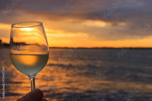 Female hand with a glass of white wine on the background of a beautiful sunset.  Travel vacations concept.