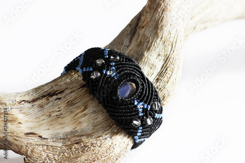 wooden curve stick and a black bracelet on the hand of waxed thread, plastic beads and moonstone in the technique of macrame.
