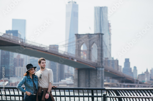 Smiling couple of friends standing in front of the Brooklyn Bridge, New York