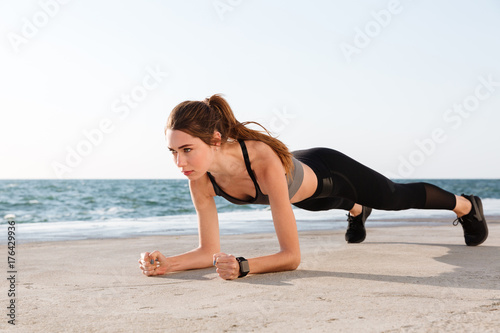 Photo of young pretty female athlete in sport wear standing in a plank position at the seaside © Drobot Dean