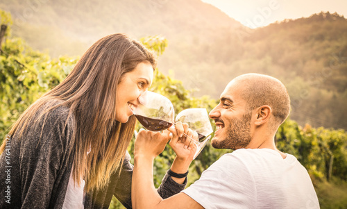 Happy young couple of lover drinking red wine at vineyard farmhouse - Handsome man looking at beautiful woman eyes - Alternative relationship concept with boyfriend and girlfriend having fun together